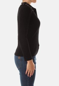 Maglione nero a coste con silhouette aderente e colletto decorato. Maniche lunghe e texture liscia. Abbinato a jeans blu.