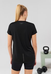 Tricou activ negru cu mâneci scurte și o deschidere la spate. Fabricat dintr-un material respirabil, are o marcaj subtil aproape de gât.