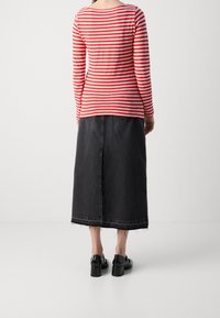 Stripet langærmet top i rød og hvid, parret med en midi-nederdel i mørkt denim med frynset kant og to baglommer. Sorte chunky hælede sko.