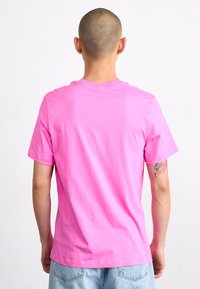 Rožinė medvilninė marškinėliai su trumpomis rankovėmis ir apvaliu kaklu, pasižymintys lygiu tekstūru ir laisvu siluetu. Gale nėra jokių iliustracijų ar raštų.