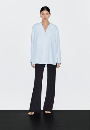 Camicia azzurro chiaro a maniche lunghe con colletto e patta frontale con bottoni, abbinata a pantaloni neri a gamba larga. Tessuto liscio e vestibilità ampia.