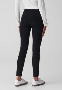 Jeans ajustados negros de mezclilla, con una cintura de altura media, bolsillos traseros y un estilo de ajuste slim. Combinados con zapatillas blancas.