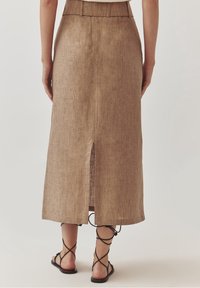 Brązowa lniana midi spódnica z tylnym rozcięciem, wyposażona w dopasowany pas. W zestawie z czarnymi sandałami na paski.