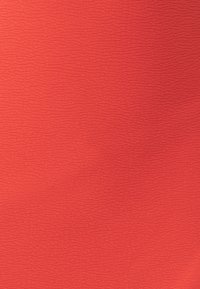 Textiel met textuur in een levendige koraalkleur, met een golvend patroon over het oppervlak, wat een visueel interessant ontwerp creëert.