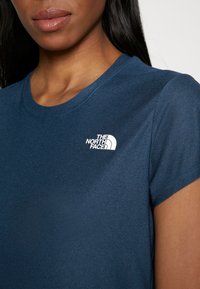 Lyhythihainen tummansininen t-paita pehmeästä kankaasta, jossa valkoinen logo vasemmalla rinnalla. Pyöreä pääntie ja sileä pinta.