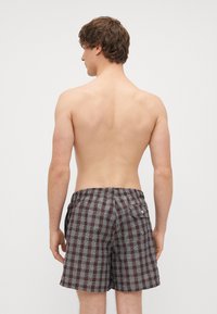 Καφέ και μπλε καρό μαγιό με ελαστική μέση και πίσω τσέπη, εμφανίζεται από πίσω σε γυμνό κορμό.