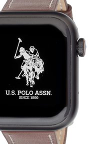 Smartwatch con display quadrato nero che presenta un logo bianco di polo. Cinturino in pelle marrone con cuciture chiare e finitura texturizzata.