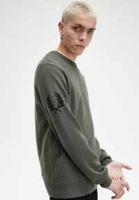 Maglione verde oliva realizzato in tessuto morbido, con colletto a girocollo e polsini a costine. Logo ricamato nero sulla manica sinistra.
