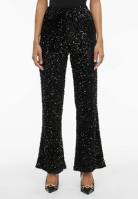 Črne hlače z bleščicami s širokimi nogavicami, teksturirane površine in visokim pasom. Kombinirane s črnimi koničastimi petami z zlato strojno opremo.