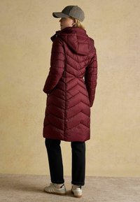 Burgundia puffer-jope, millel on v-diagonaal stitch ja kapuuts. Sobitatud mustade teksade ja valgete tennisetossudega. Mütsil on ruuduline muster.