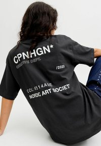 Sort oversized T-shirt med hvid tekst, herunder "CPNHGN," "CREATIVE DEPT.," og "NORDIC ART SOCIETY" på ryggen.