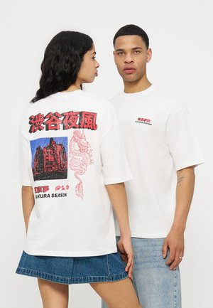 To modeller bærer hvide "SAKURA SEASON" t-shirts, den ene viser ryggen med grafik af en rød drage og en bygning, den anden fronten med lille rød tekst.