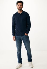 Marineblaues Poloshirt mit langen Ärmeln aus weichem Stoff, mit einem klassischen Kragen, kombiniert mit hellblauen Jeans und weißen Sneakern.