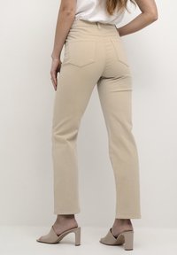 Pantaloni beige a vita alta con vestibilità slim, dotati di tasche posteriori e design a gamba dritta. Tessuto morbido con una sottile texture.