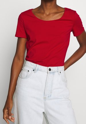 Rood katoenen T-shirt met korte mouwen en een ronde hals, gecombineerd met lichtblauwe hoogwater spijkerbroeken met voorzakken en knopen.