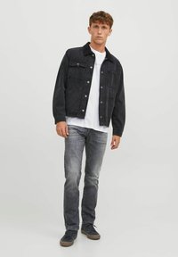 Jachetă din denim închis cu nasturi metalici și două buzunare pe piept, asortată cu blugi gri deschis și pantofi sport negri. Tricou alb dedesubt.