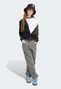 Black velvet zip-up jacket over a white shirt, gray elastic waist pants, and blue sneakers, paired with a black bucket hat.