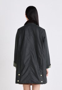 Dark green waterproof coat with a collar, featuring gold accents, a straight cut, and button details on the back and sleeves.