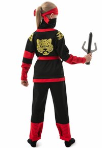 Ninja-Kostüm aus schwarzem Stoff mit roten Akzenten und einem goldenen Tiger-Graphic. Enthält ein passendes Stirnband und ein Kunststoffwaffen-Zubehör.