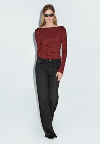 Maglietta a maniche lunghe rossa e nera a righe con scollatura ampia abbinata a jeans neri in denim a vita alta. Gli occhiali e il taglio dritto accentuano il look.