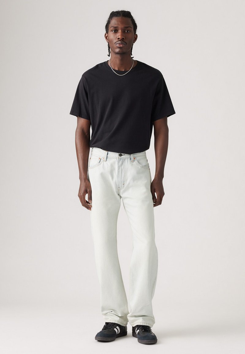 Camiseta negra de manga corta combinada con jeans azul claro. Los jeans tienen un corte holgado y detalles de costura sutiles. Zapatillas negras completan el look.