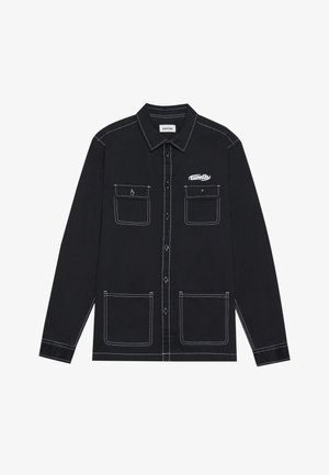 Črna majica z dolgimi rokavi z dvema žepoma na prsih, kontrastno belo šivanje in zapenjanje spredaj na gumb. Ima koničast ovratnik in logotip blagovne znamke.