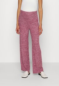 Breda ben, rosa melerade byxor med en mjuk textur och elastisk midja, tillsammans med vita slip-on skor.