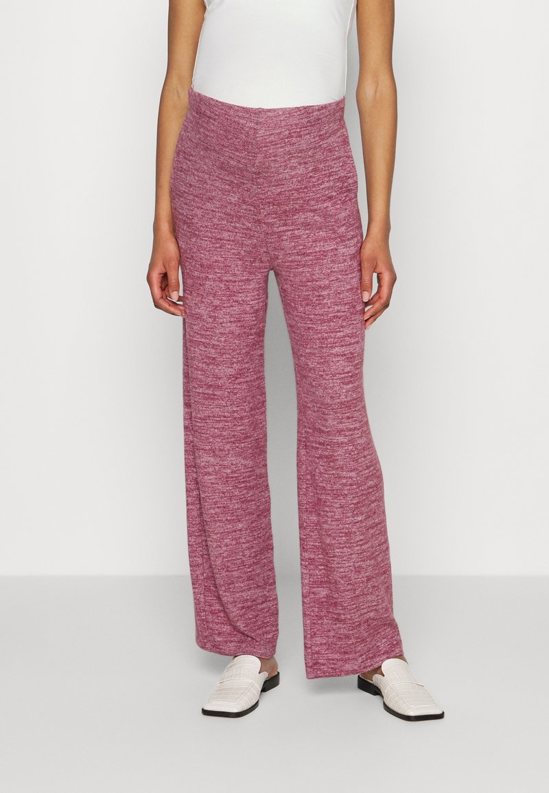 Breda ben, rosa melerade byxor med en mjuk textur och elastisk midja, tillsammans med vita slip-on skor.