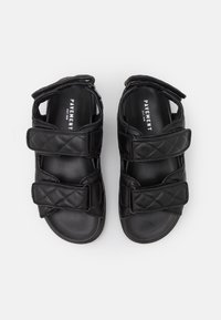 Sandales noires matelassées avec deux brides réglables en Velcro, design ouvert à l'avant, et semelle lisse. Marquées "PAVEMENT" à l'intérieur de la semelle.