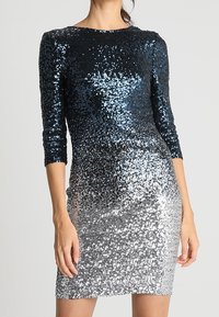 Paljetklänning med trekvartslånga ärmar; gradient från mörkblått högst upp till silver vid fållen. Har en figurnära silhuett och mjuk textur.