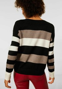 Randig tröja i svart, vitt och beige med avslappnad passform och ribbad halsringning; bärs med röda läderbyxor och visar bakifrån.