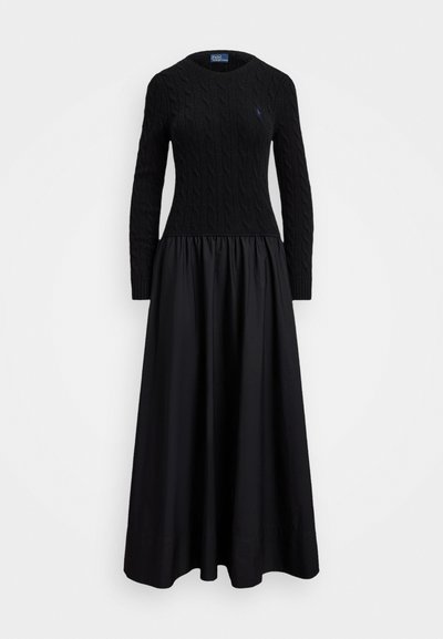 Musta mekko, jossa on teksturoitu pylväsknitti yläosa ja virtaava, kerätty hame. Pyöreä kaula-aukko ja pitkät hihat.