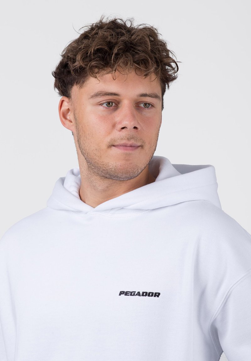 Weißer Hoodie aus weichem Stoff, mit einer vorderen Kängurutasche und einem kleinen schwarzen "PEGADOR"-Logo auf der linken Seite.