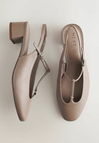 Escarpins beige à bride arrière avec un petit talon carré, design ajouré, bride de cheville réglable et texture en cuir lisse. Logo sur la semelle intérieure.