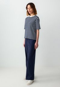 Top rayé bleu marine et blanc à manches courtes associé à un pantalon large bleu marine uni. Le modèle porte des baskets blanches. Tenue simple et décontractée.