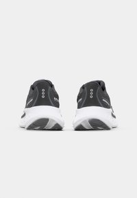 Baskets de sport noires avec un talon gris, une semelle intermédiaire blanche et une marque discrète. Elles présentent un design texturé et des trous de ventilation.