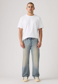 Τζιν παντελόνια από ανοιχτό μπ λε τζιν με ξεθωριασμένο φινίρισμα, συνδυασμένα με απλό λευκό μπλουζάκι και κρεμ αθλητικά παπούτσια. Σχεδίαση με ίσια μπατζάκια, ελάχιστες λεπτομέρειες.