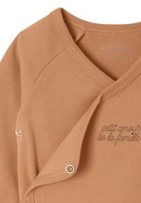Sandfarbener Baumwoll-Longsleeve-Overall mit V-Ausschnitt, Druckknopfverschlüssen und dem aufgedruckten Text "petit amour de la famille" in der Nähe der Öffnung.