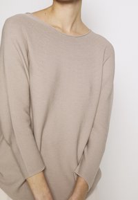 Beige gebreid sweater met driekwartmouwen en een ruime halslijn. De textuur is zacht en licht geribbeld, wat een casual uitstraling geeft.