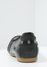 Czarna skórzana szpilka z teksturowanym wykończeniem, metalowymi ćwiekami na pięcie i gładkim, okrągłym kształtem. Gumowa podeszwa zapewniająca przyczepność.