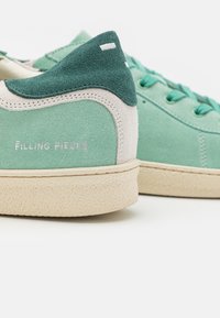 Sneakers verde in suede con accenti crema e suole testurizzate. Presentano il marchio "Filling Pieces" sul lato e un design con lacci.