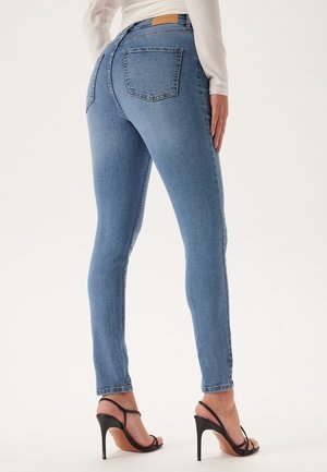 Slim-fit jasnoniebieskie dżinsy z przeszyciami, dwoma tylnymi kieszeniami i średnim stanem, zestawione z czarnymi sandałami na obcasie.