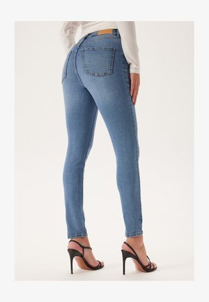 Slim-fit lichtblauwe spijkerbroek met gestikte details, twee achterzakken en een midi-riser taille, gecombineerd met zwarte hak sandalen.