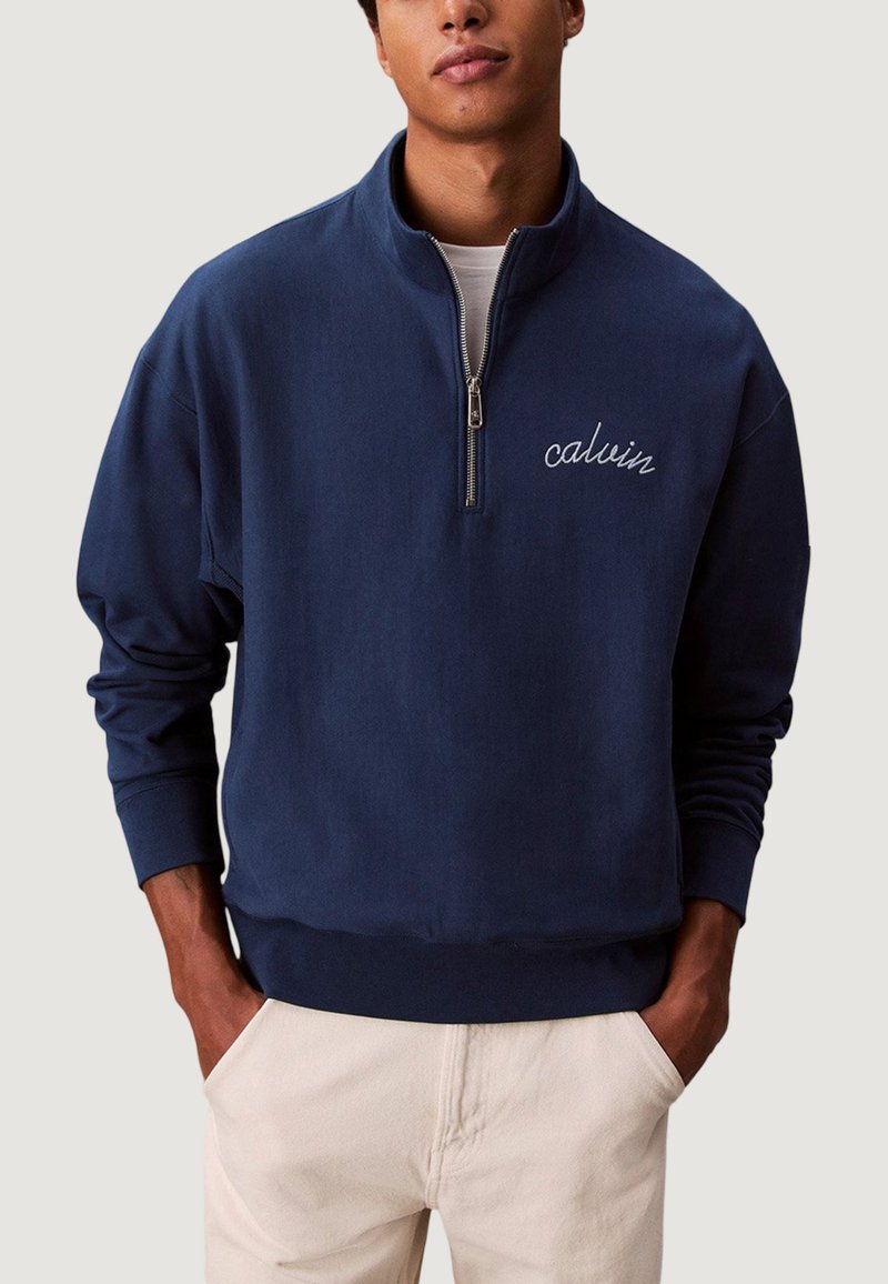 Sudadera azul marino con cremallera, cuello alto y logo "calvin" bordado. Fabricada con tejido suave, presenta un corte relajado y puños acanalados.