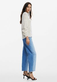 Maglione grigio chiaro a maglia con puntini multicolori, abbinato a jeans in denim larghi a vita alta e sandali neri con tacco a strappo.
