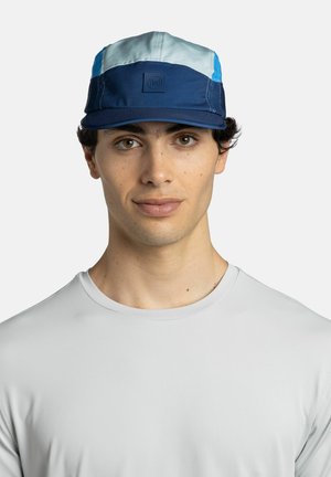 Young man wearing a blue and light blue cap and a plain light grey crew neck shirt, facing forward against a white background.