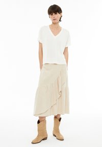 Top de punto blanco de manga corta y escote en V, combinado con una falda de canalé beige con un dobladillo con volantes, complementado por botas de cowboy marrón claro.