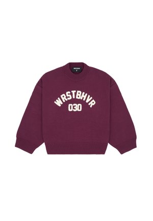 Pullover bordeaux surdimensionné avec le texte blanc "WRSTBHV" et "030" ; assorti d'une mini-jupe noire matelassée et de talons aiguilles noirs.