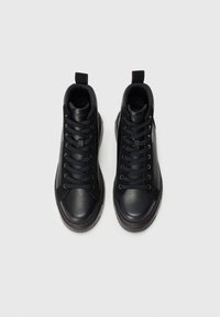 Zapatillas altas negras de cuero con un acabado suave. Presentan cordones negros, acentos en el panel lateral y costuras rojas a lo largo de la suela.