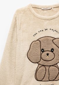 Tan fleece top featuring a cartoon dog design in brown. The text above reads, "you can be anything." Soft, plush texture. Round neckline.